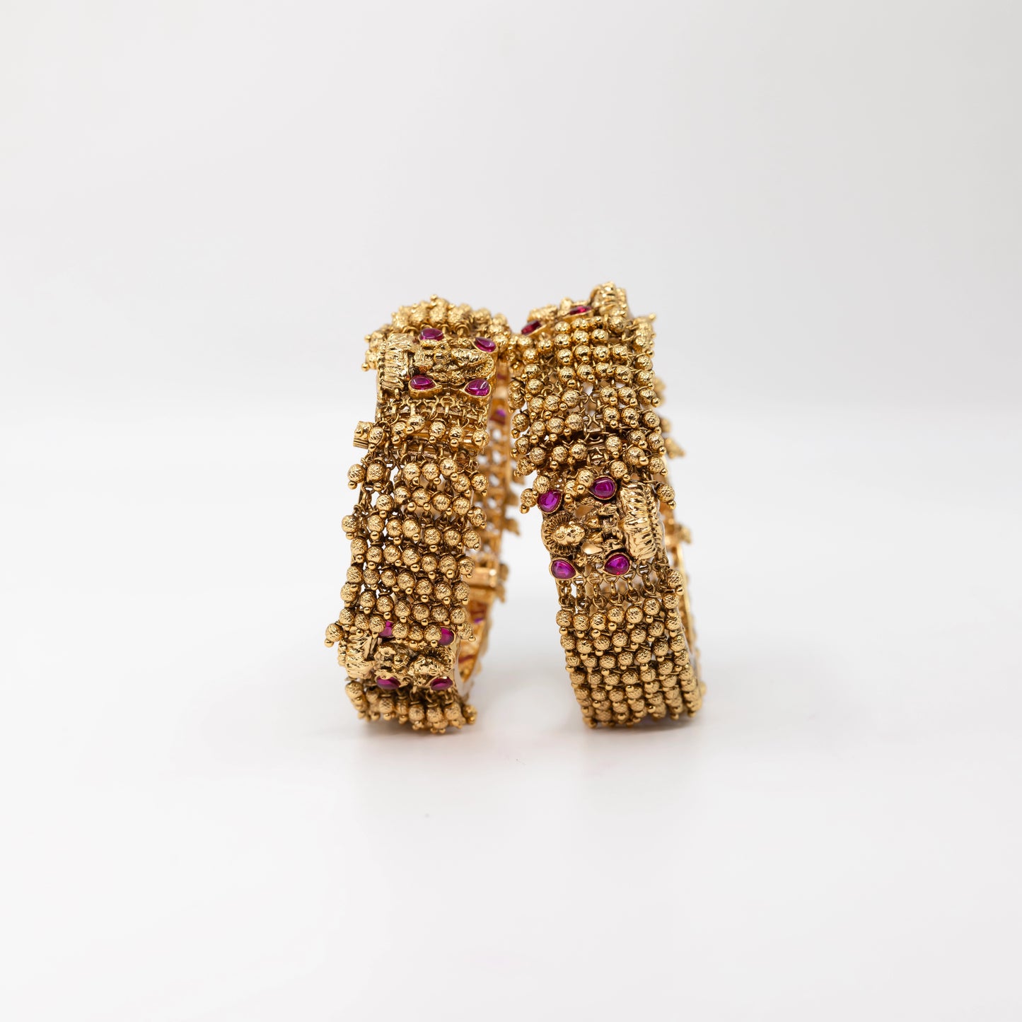 Gold Ball Bangle with red gemstones on a textured surface