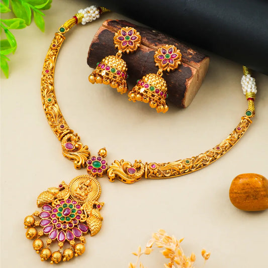 Gold necklace with floral designs and colorful stones on a light background