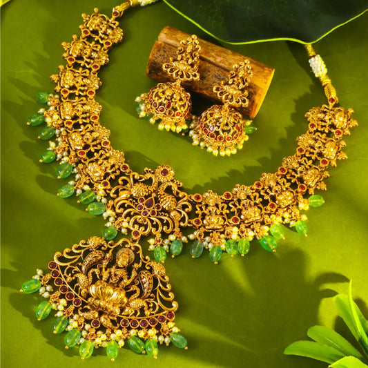 Lakshmi Gold necklace with green stones on a green leaf background