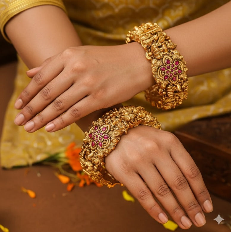 Close-up of hands wearing ornate gold bracelets with pink stones on a blurred background.